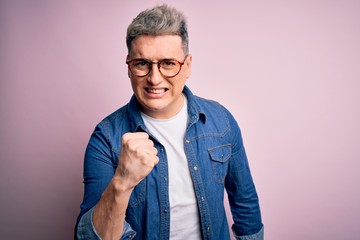 Young handsome modern man wearing glasses and denim jacket over pink isolated background angry and mad raising fist frustrated and furious while shouting with anger. Rage and aggressive concept.