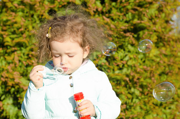 portrait little beautiful girl blows soap bubbles. happy child plays outside. baby plays outdoors...