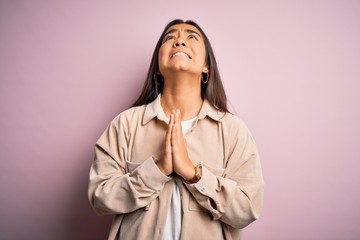 Young beautiful asian woman wearing casual shirt standing over pink background begging and praying...