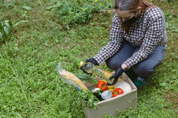 Woman delivering donations box with food during Covid 19 outbreak.Feme volunteer collects food in a box standing on the grass