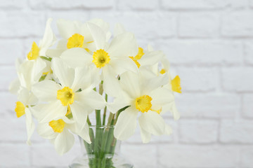 Vase of white and yellow daffodil flowers with white brick as background