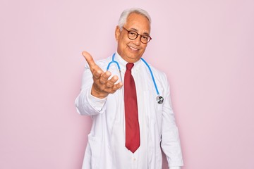 Middle age senior grey-haired doctor man wearing stethoscope and professional medical coat smiling cheerful offering palm hand giving assistance and acceptance.