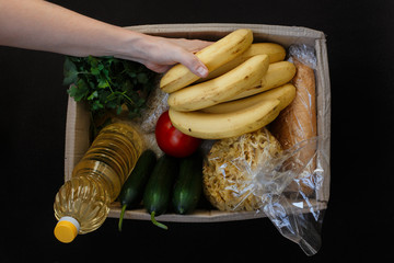 Valanter's hand in protective gloves fill the box with food on a black background.Donation concept....