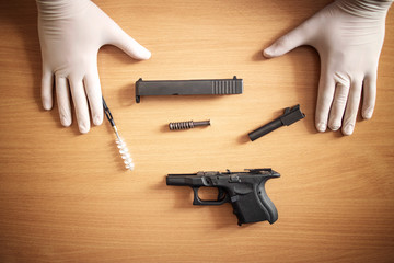 Firearm cleaning and maintenance after use at shooting range. Handgun disassembled into parts and brush for cleaning gunpowder residue. - obrazy, fototapety, plakaty