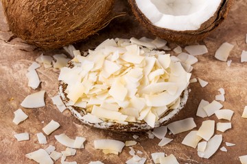 Health content, whole coconut, coconut half, coconut flakes in plate, brown background, top view