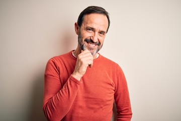 Middle age hoary man wearing casual orange sweater standing over isolated white background looking confident at the camera smiling with crossed arms and hand raised on chin. Thinking positive.