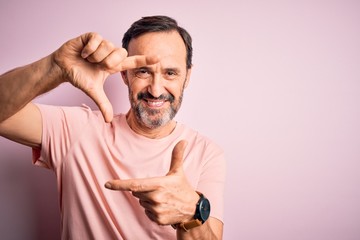 Middle age hoary man wearing casual t-shirt standing over isolated pink background smiling making frame with hands and fingers with happy face. Creativity and photography concept.