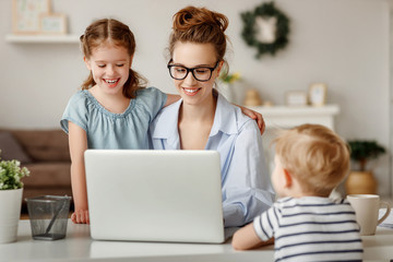 Little children distracting dedicated young woman working on laptop at home