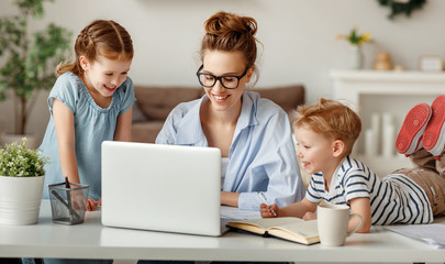 Little children distracting dedicated young woman working on laptop at home