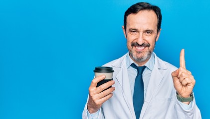 Middle age handsome doctor man wearing coat drinking cup of takeaway coffee smiling with an idea or question pointing finger with happy face, number one