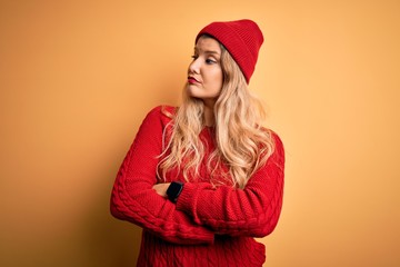 Young beautiful blonde woman wearing casual sweater and wool cap over white background looking to the side with arms crossed convinced and confident