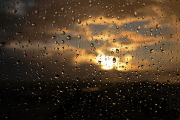 Regentropfen an einer Glasscheibe. Im Hintergrund der Sonnenuntergang.