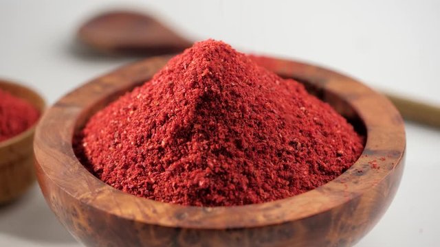Red chili powder or paprika in a wooden bowl rotation on a white background, close-up. Cooking ingredients, flavor.