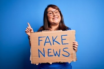 Beautiful plus size woman holding fake news banner for false journalism over isolated background...