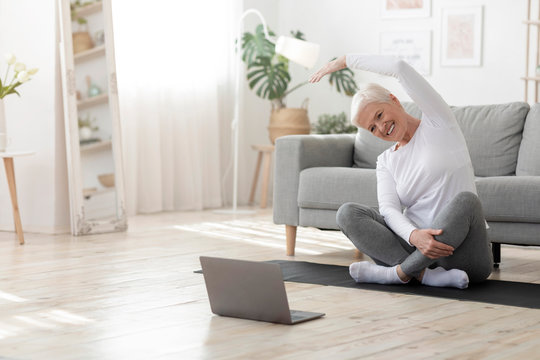 Happy senior woman doing stretching exercises in front of laptop at home