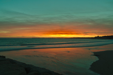 Fototapeta na wymiar Beautiful Sunset, Orange and Turquoise Reflecting off the sea and waves down on the beach at El Puerto de Santa Maria