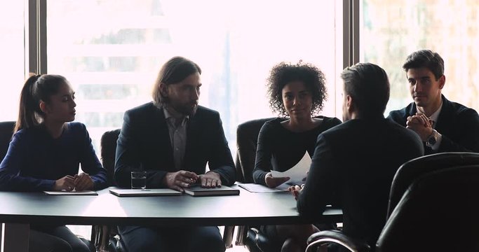 Confident male leader of diverse human resource management team holding job interview with candidate. Skilled smart applicant sharing working experience with employers, first impression concept.