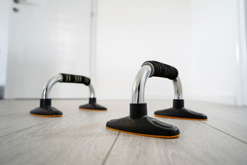close up on metal shiny push up bars with black handle and base training equipment on the wooden floor at home in day