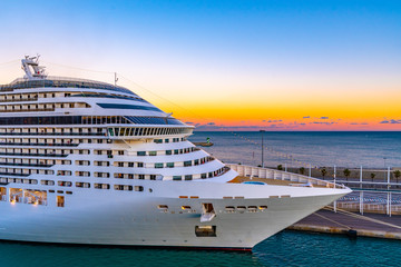 Front/ Bow of Cruise Ship docked/ anchored/ moored in Port. Colorful sunset sky glow on horizon in background.