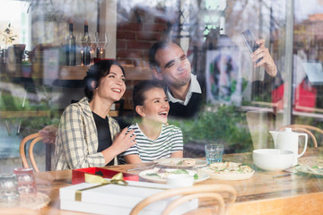 Fototapeta na wymiar A happy family of three making selfies in a cafe