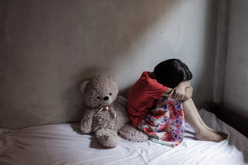 Sad little girl with bear toy sitting in room. traumatized children concept