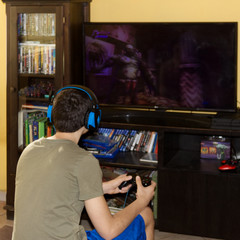 Caucasian boy with headphones, sitting in an armchair, playing a video game with the console