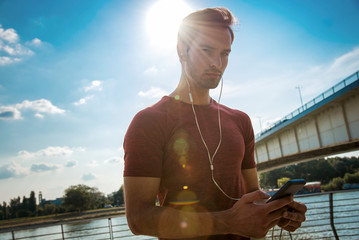 Attractive young fitness guy listening to his music on his phone