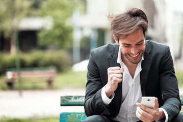 Attractive young businessman holding his phone, reading a message and looking astonished