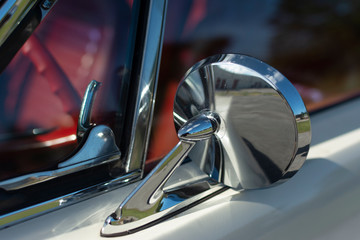 Chrome mirror of an old American muscle car. White classic car with red interior.