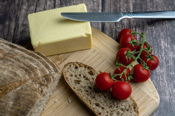 Sliced bread, butter, tomatoes, salt and knife on a wooden board. Color food photography.