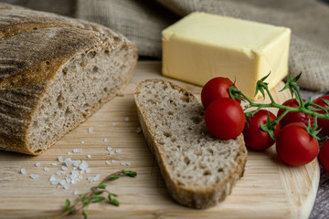 Sliced bread, butter, tomatoes, salt and herbs  on a wooden board. Color food photography.