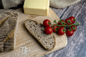 Sliced bread, butter, tomatoes, salt and herbs  on a wooden board. Color food photography.
