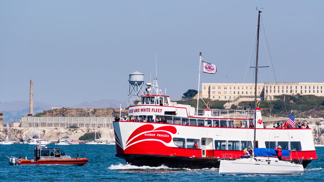 Oct 12, 2019 San Francisco / CA / USA - A US Coast Guard boat approaching a Red and White Fleet sightseeing ship cruising in the San Francisco Bay; Alcatraz island visible in the background