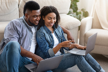 Obraz premium Quarantine Life. Happy Black Couple Sitting With Laptops On Floor At Home