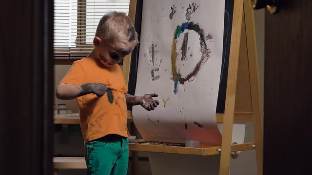 Cute child (Caucasian boy) is having fun, painting in his room. Kids dirty face and shirt after art activities. Fun activity for kids indoor, parenting  concept
