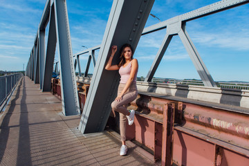 Pretty young woman posing on the old rusty transport bridge over the river during sunset.