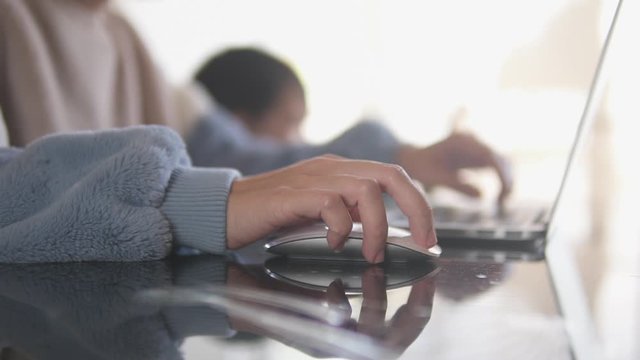 Slow motion video of a young millennial mother working from home using the mouse on a laptop at her home office and taking care of her son watching cartoon on a tablet