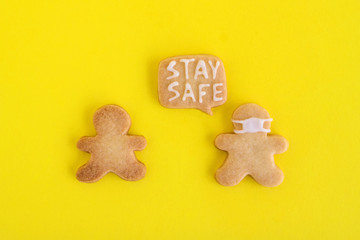 Homemade shortbread cookies with white glaze on yellow background, top view. Two men one of them in face mask and with callout cloud with text ‘Stay safe’.