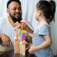 Father watching his Little Girl Playing Wooden Block Toy at Home.
