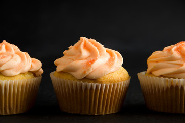 Close-up of Delicious Orange Muffins with Icing and Sugar on Dark Background