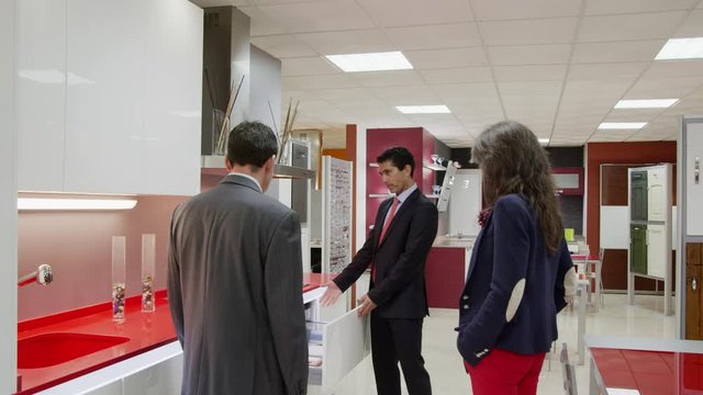 WS DS TS Salesman showing kitchen furniture to couple in kitchen showroom