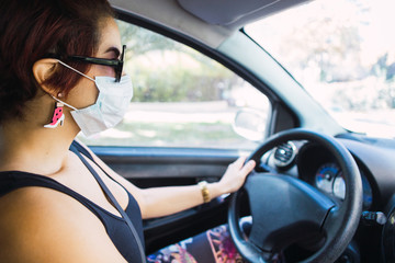 Young woman transporting herself in her car to work wearing a face mask during the corona virus pandemic.