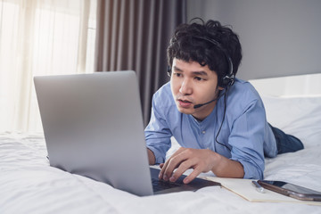 business man wear headset video conference calling on laptop computer on bed, work from home concept