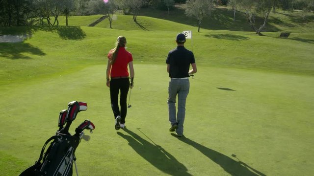 WS TS DS Two golfers on putting green, man taking shot and misses