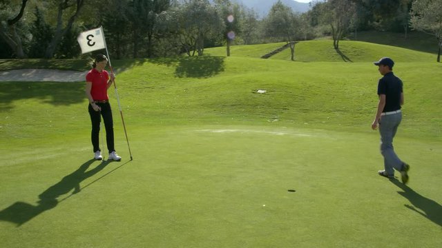 WS&nbsp;TS&nbsp;DS&nbsp;Golfers on putting green, woman taking shot and ball falls into hole