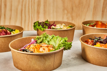 Traditional organic poke bowl of salmon, shrimp, avocado, rice, vegetables placed on textured backgrounds ready to eat.