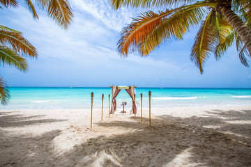 Colorful wedding arch gazebo pavilion made of bamboo and textile with fresh flowers decoration at sandy beach on sunny day for destination wedding ceremony in Dominican republic  