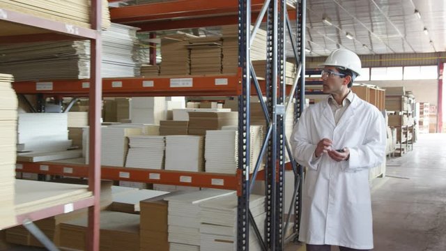 WS&nbsp;DS&nbsp;TS Man in lab coat and hardhat walking in furniture factory warehouse