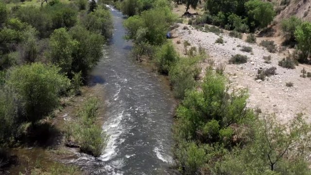 Aerial above flowing clean river wilderness between woodland trees