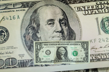 Hay un billete de un dólar y de fondo hay un billete de cien dólares americanos.